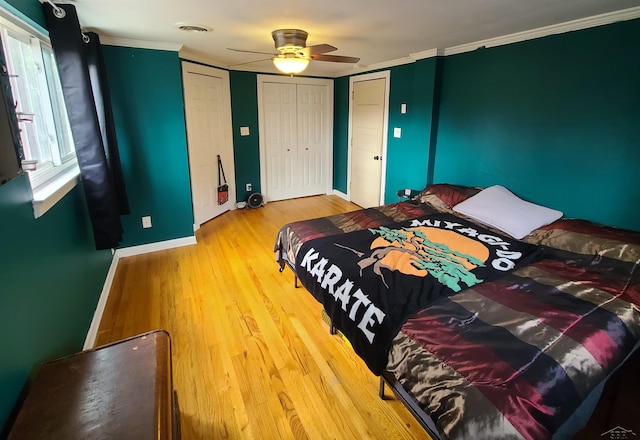 bedroom featuring ceiling fan, two closets, wood-type flooring, and ornamental molding