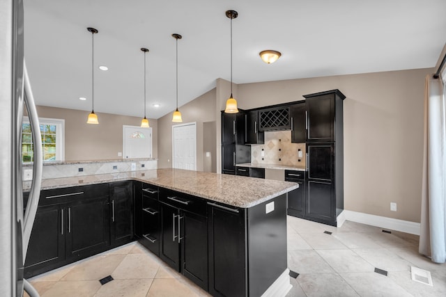 kitchen with decorative backsplash, stainless steel fridge, light stone counters, vaulted ceiling, and hanging light fixtures