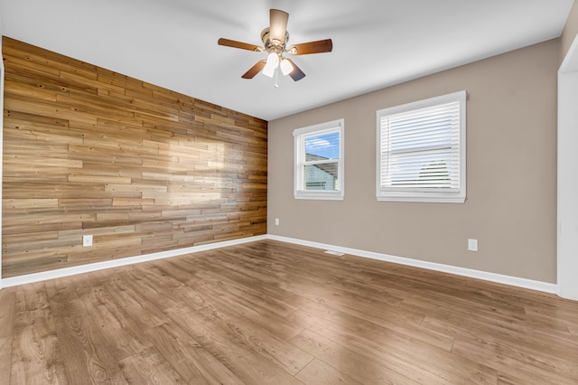 spare room with light hardwood / wood-style floors, ceiling fan, and wooden walls