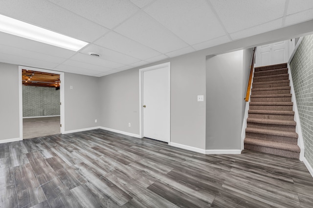 basement with hardwood / wood-style floors, a drop ceiling, and brick wall