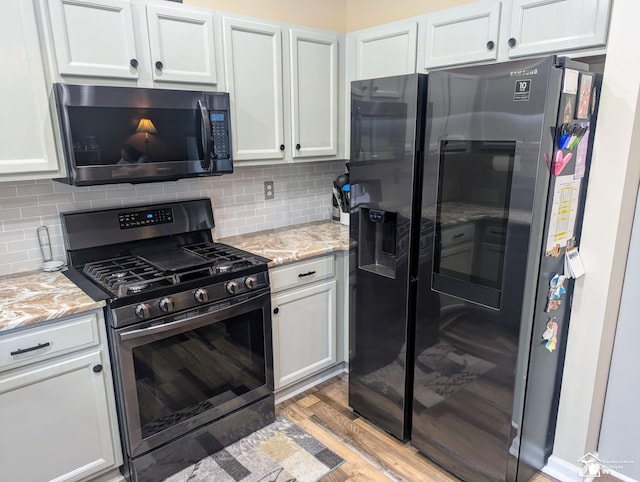 kitchen featuring decorative backsplash, light hardwood / wood-style floors, light stone counters, white cabinetry, and stainless steel appliances