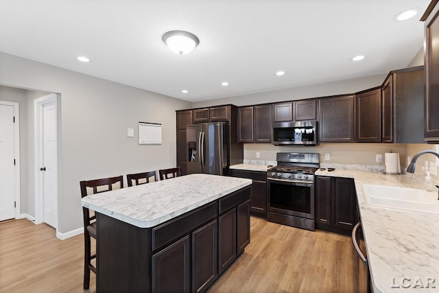 kitchen with appliances with stainless steel finishes, a kitchen breakfast bar, sink, light hardwood / wood-style flooring, and a kitchen island