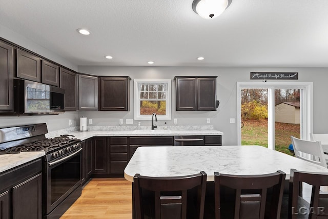 kitchen featuring a kitchen bar, light wood-type flooring, dark brown cabinets, stainless steel appliances, and sink