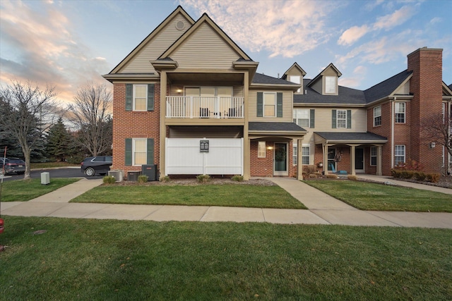 view of front of house featuring a balcony, a lawn, and central air condition unit