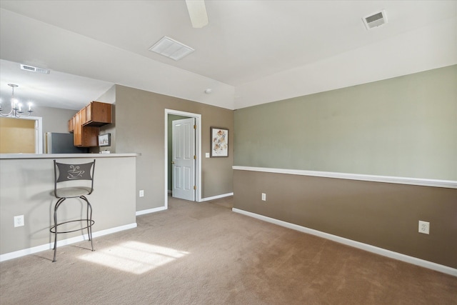 kitchen with a kitchen breakfast bar, an inviting chandelier, light colored carpet, and fridge