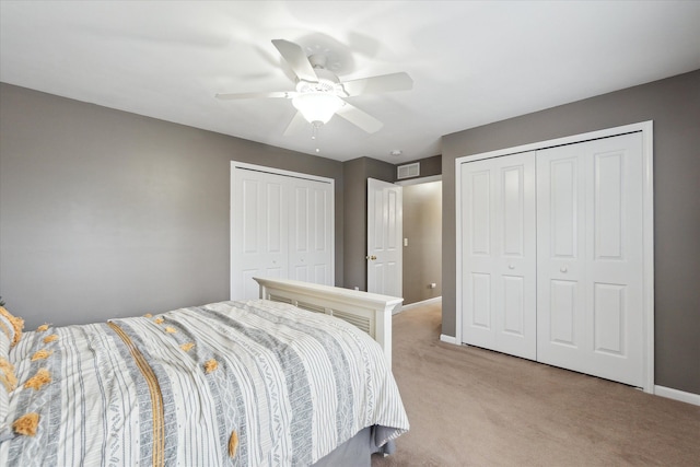 bedroom with ceiling fan, light carpet, and multiple closets