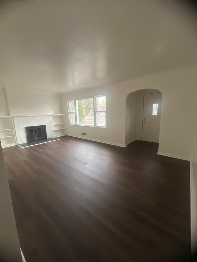 1060 Cross St, Saginaw, MI 48602 - unfurnished living room with arched walkways, dark wood-style flooring, baseboards, and a glass covered fireplace