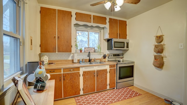 kitchen with ceiling fan, sink, backsplash, appliances with stainless steel finishes, and light wood-type flooring