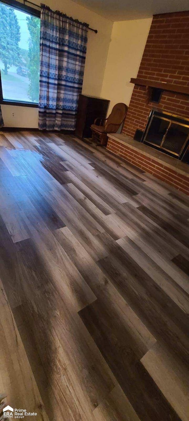 unfurnished living room featuring dark wood-type flooring and a brick fireplace