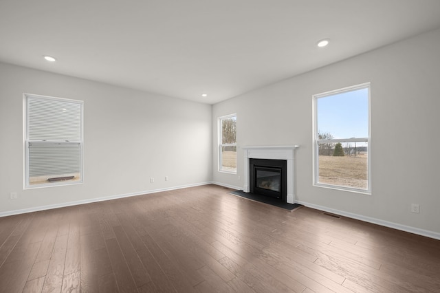 unfurnished living room featuring visible vents, dark wood-type flooring, baseboards, recessed lighting, and a glass covered fireplace