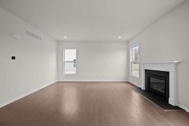 unfurnished living room with dark wood-style floors, visible vents, baseboards, recessed lighting, and a glass covered fireplace