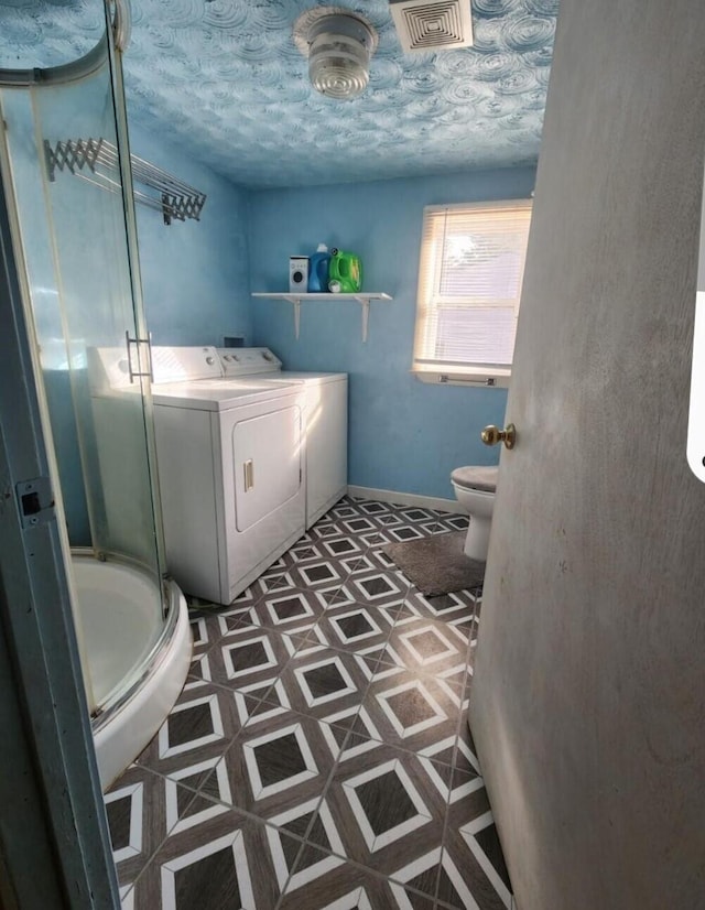 bathroom with tile patterned flooring, washer and dryer, an enclosed shower, and toilet