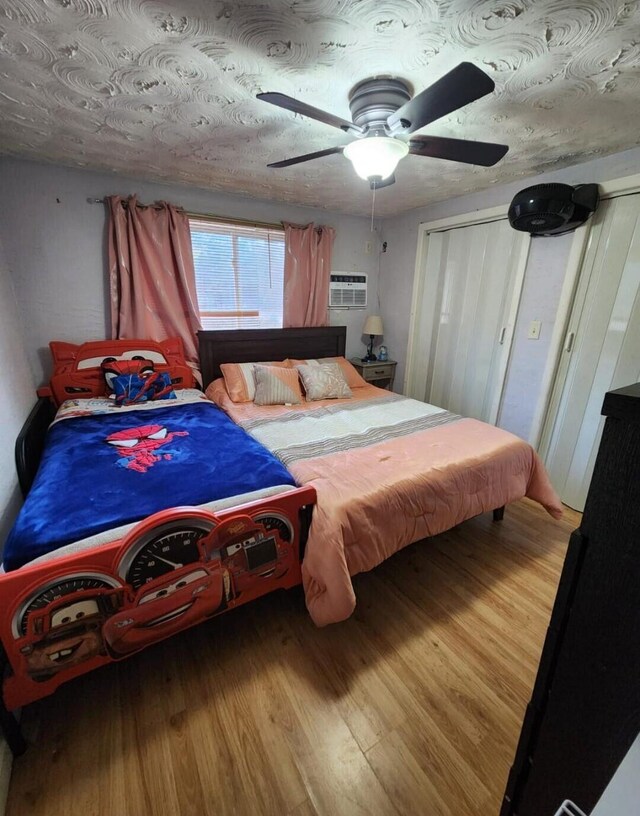 bedroom with hardwood / wood-style flooring, an AC wall unit, and ceiling fan