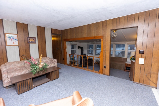 carpeted living room featuring wooden walls and a wood stove