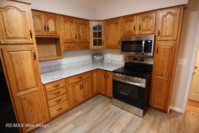 kitchen with light stone countertops, light wood-type flooring, and appliances with stainless steel finishes