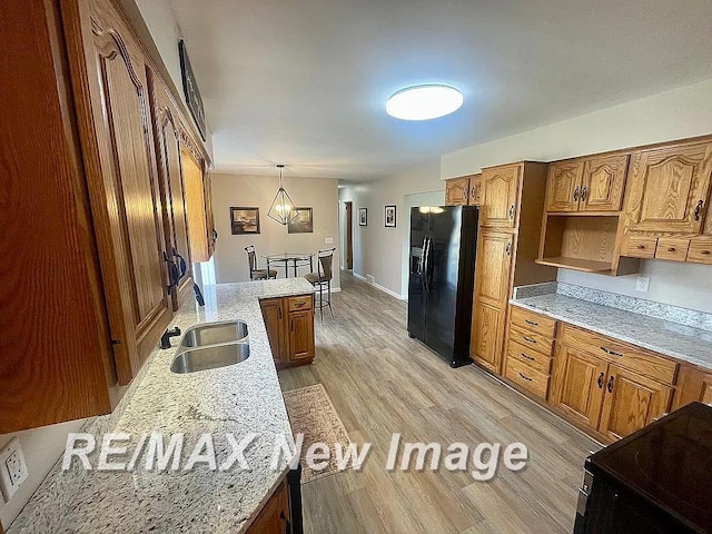 kitchen with light stone countertops, black fridge with ice dispenser, decorative light fixtures, and sink