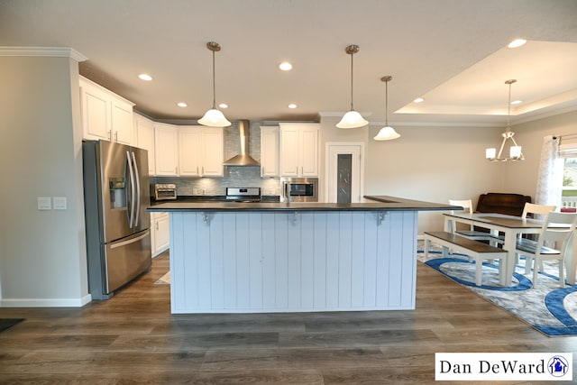 kitchen with appliances with stainless steel finishes, pendant lighting, white cabinetry, a kitchen island with sink, and wall chimney exhaust hood