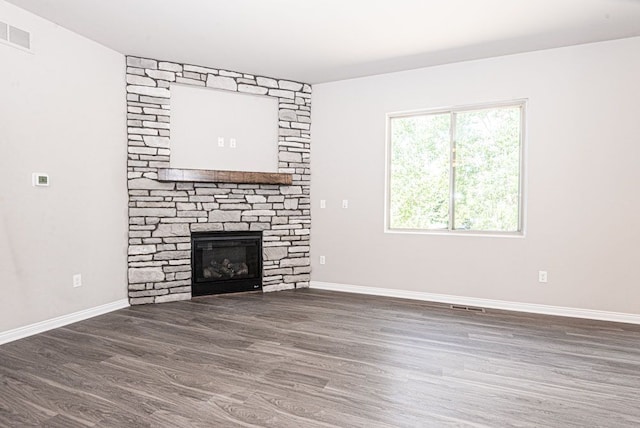 unfurnished living room featuring a stone fireplace and dark wood-type flooring