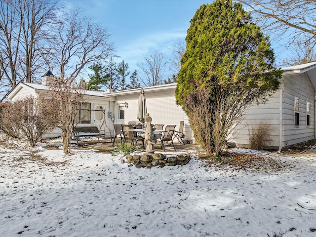 snow covered back of property with a patio