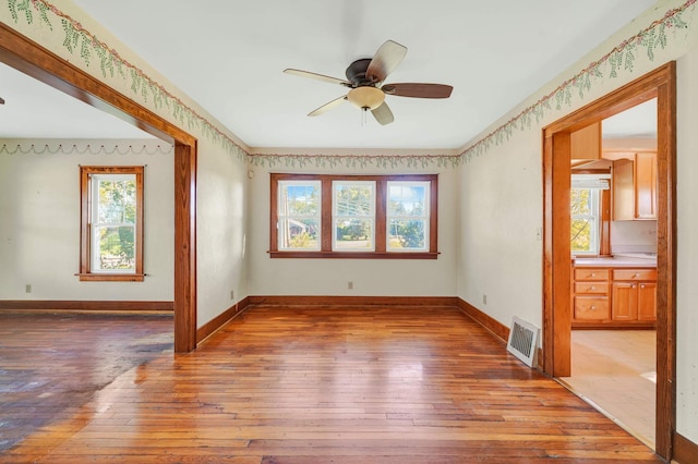 empty room with a wealth of natural light, ceiling fan, and wood-type flooring