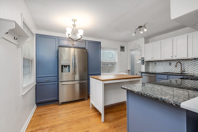 kitchen with blue cabinetry, wood counters, hanging light fixtures, light hardwood / wood-style flooring, and appliances with stainless steel finishes