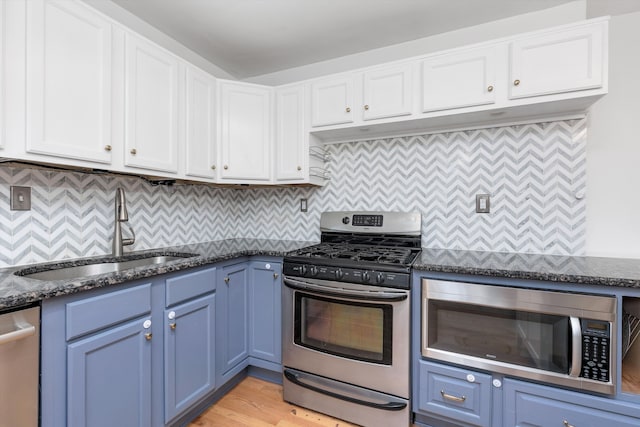 kitchen with stainless steel appliances, blue cabinets, sink, and dark stone countertops