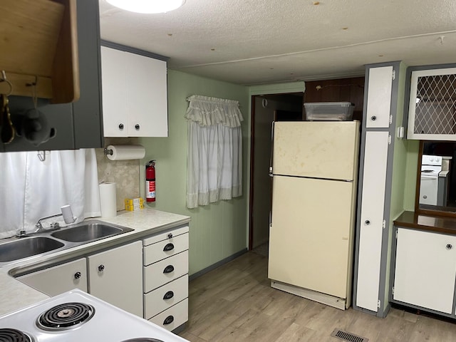 kitchen with white fridge, white cabinetry, sink, and light hardwood / wood-style flooring