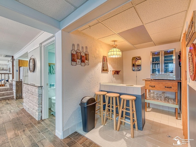 11477 Highland Hills Dr, Jerome, MI 49249 - indoor dry bar with freestanding refrigerator, a drop ceiling, a textured wall, wood finish floors, and stairway