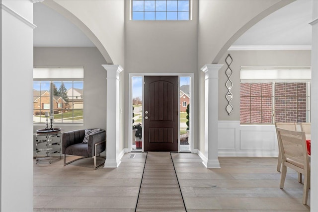 foyer featuring decorative columns, crown molding, and light hardwood / wood-style floors