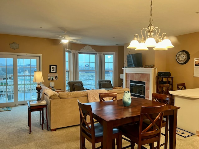 dining room with a wealth of natural light, a fireplace, light carpet, and ceiling fan with notable chandelier