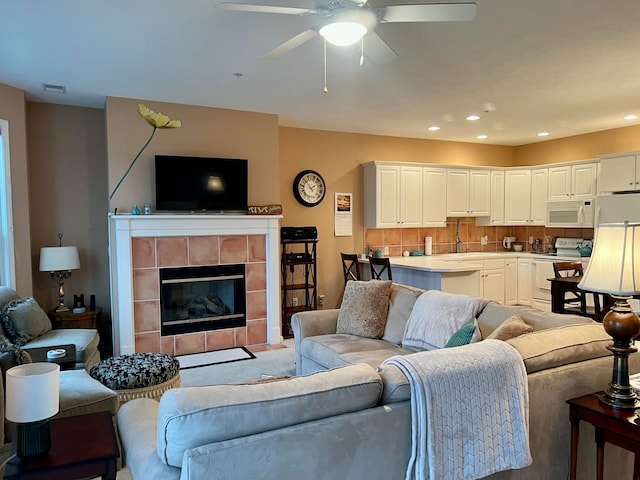 living room featuring sink, ceiling fan, and a tiled fireplace