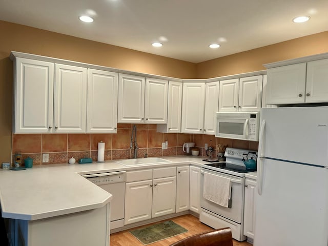 kitchen featuring white appliances, white cabinets, sink, light hardwood / wood-style flooring, and kitchen peninsula