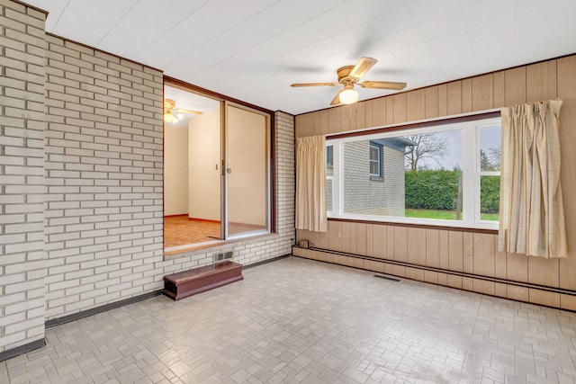 unfurnished room with ceiling fan, wood walls, baseboard heating, and brick wall