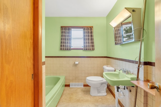 bathroom featuring sink, a bath, tile patterned floors, toilet, and tile walls