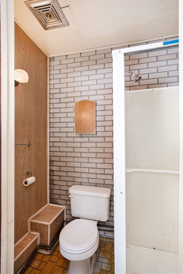 bathroom featuring brick wall and toilet