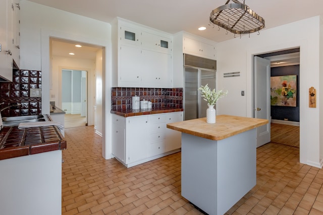 kitchen featuring tasteful backsplash, tile countertops, decorative light fixtures, white cabinetry, and built in fridge