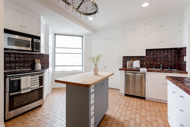 kitchen with sink, white cabinets, backsplash, a kitchen island, and appliances with stainless steel finishes