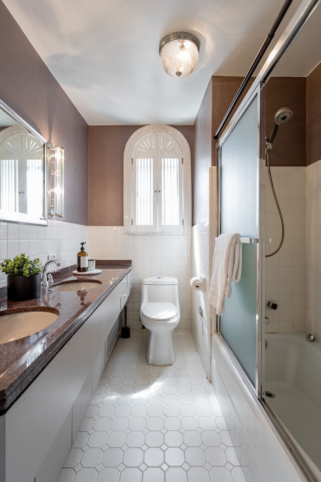 full bathroom with shower / bath combination with glass door, vanity, tile walls, and toilet