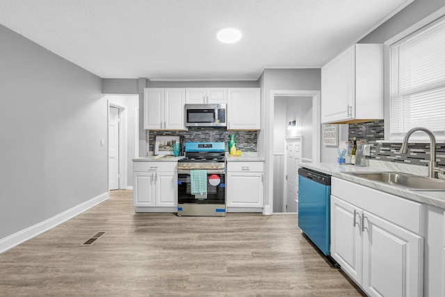 kitchen featuring tasteful backsplash, sink, white cabinets, light hardwood / wood-style floors, and stainless steel appliances