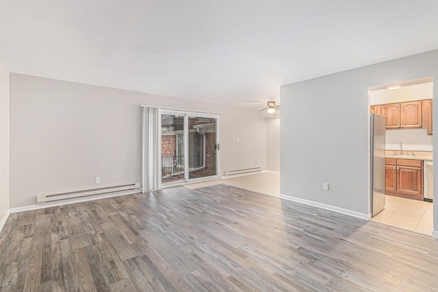 unfurnished living room featuring baseboard heating, ceiling fan, sink, and light wood-type flooring