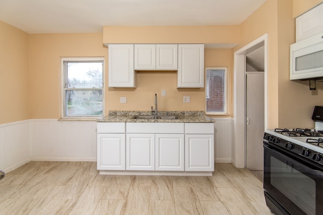 kitchen with black gas range, light stone countertops, sink, and white cabinets