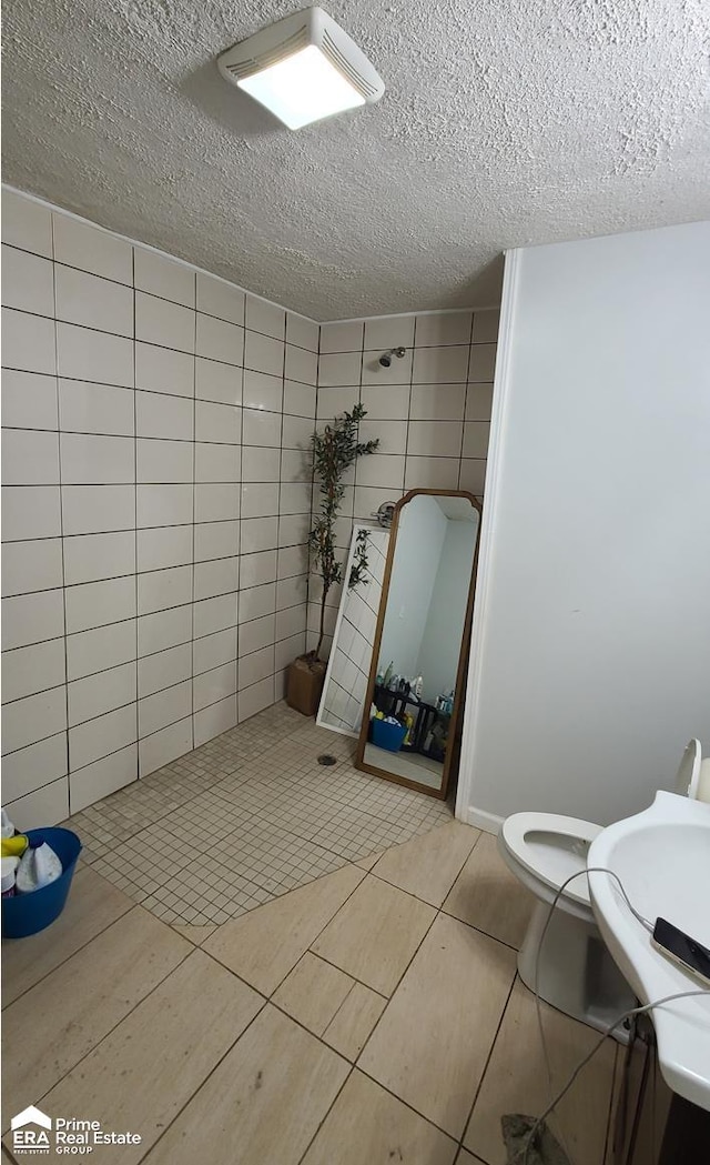 bathroom with tile patterned flooring, a textured ceiling, toilet, and tile walls