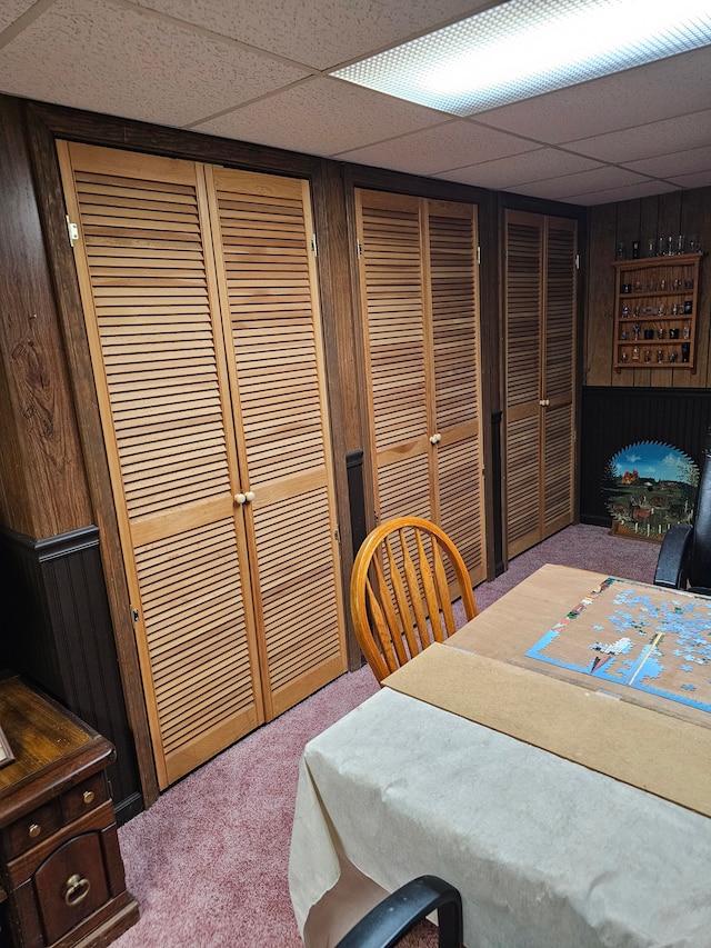 interior space with a drop ceiling, carpet floors, and wooden walls