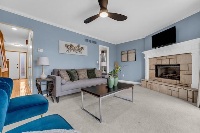 carpeted living room with a stone fireplace, ceiling fan, and ornamental molding