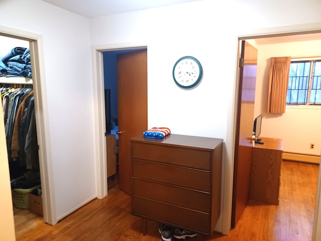 corridor with a baseboard heating unit and hardwood / wood-style flooring