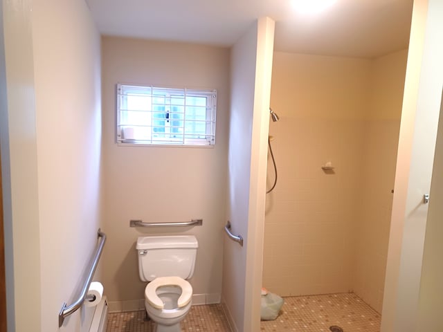 bathroom with toilet, tiled shower, and tile patterned floors