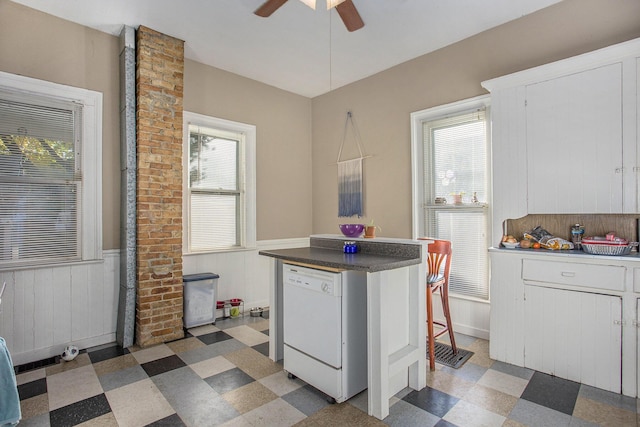 kitchen with white dishwasher, ceiling fan, white cabinets, and wood walls