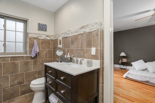 bathroom featuring vanity, ceiling fan, hardwood / wood-style flooring, tile walls, and toilet