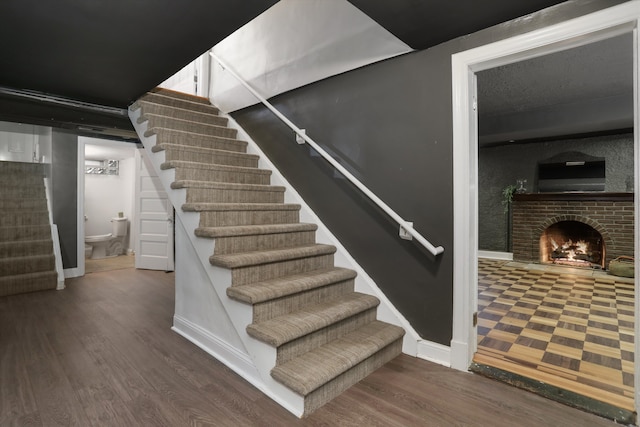 stairway with a brick fireplace and hardwood / wood-style flooring