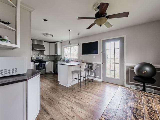 kitchen featuring appliances with stainless steel finishes, decorative light fixtures, a wealth of natural light, and wall chimney range hood